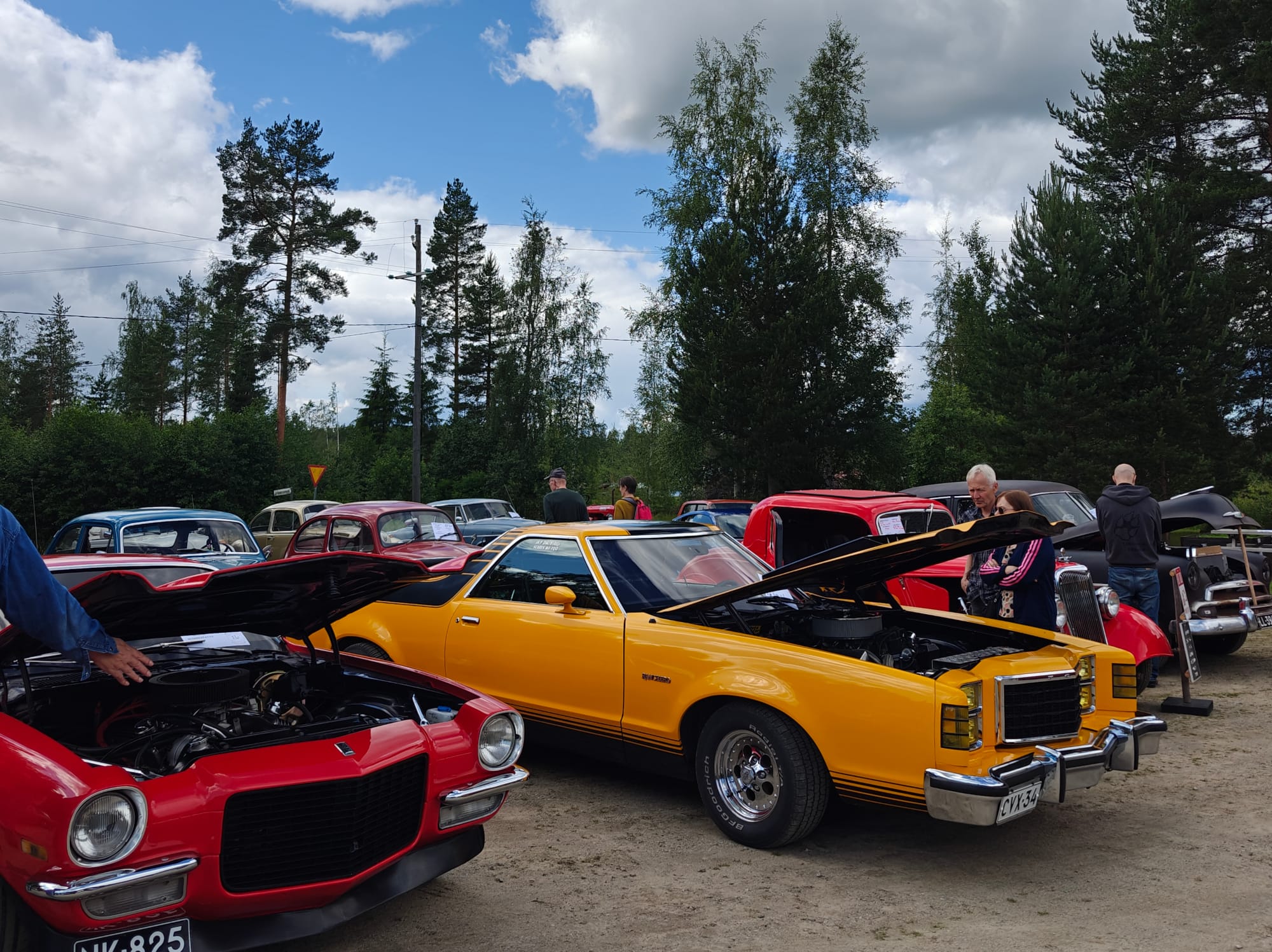 Vanhoja autoja konepellit auki ja miehiä autojen ympärillä.