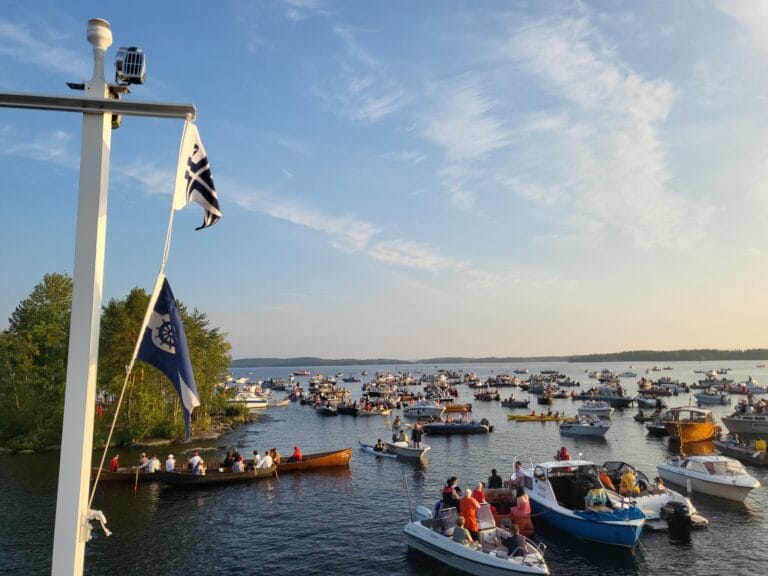 Järvimaisema, jossa paljon veneitä kerääntyneenä saaren rantaan.