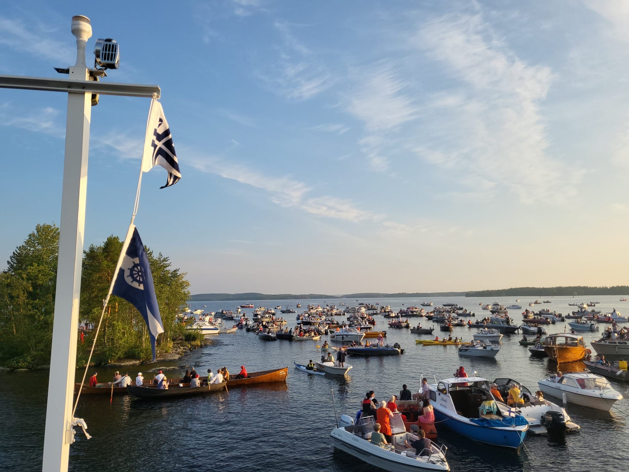 Järvimaisema, jossa paljon veneitä kerääntyneenä saaren rantaan.