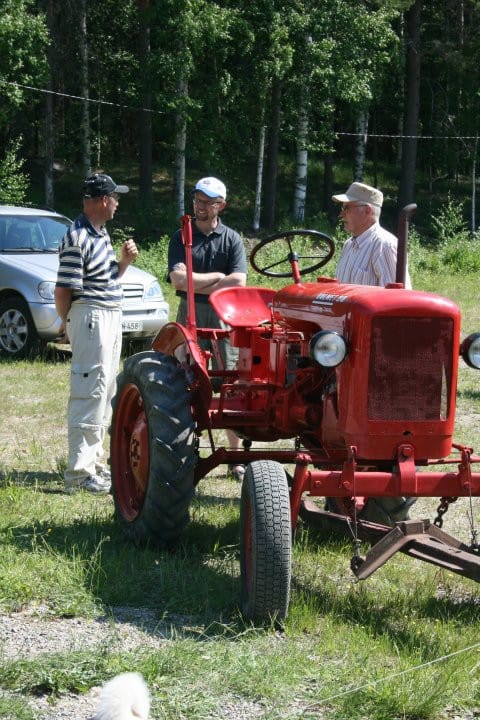 Kolme miestä kerääntyneet vanhan traktorin ympärille.
