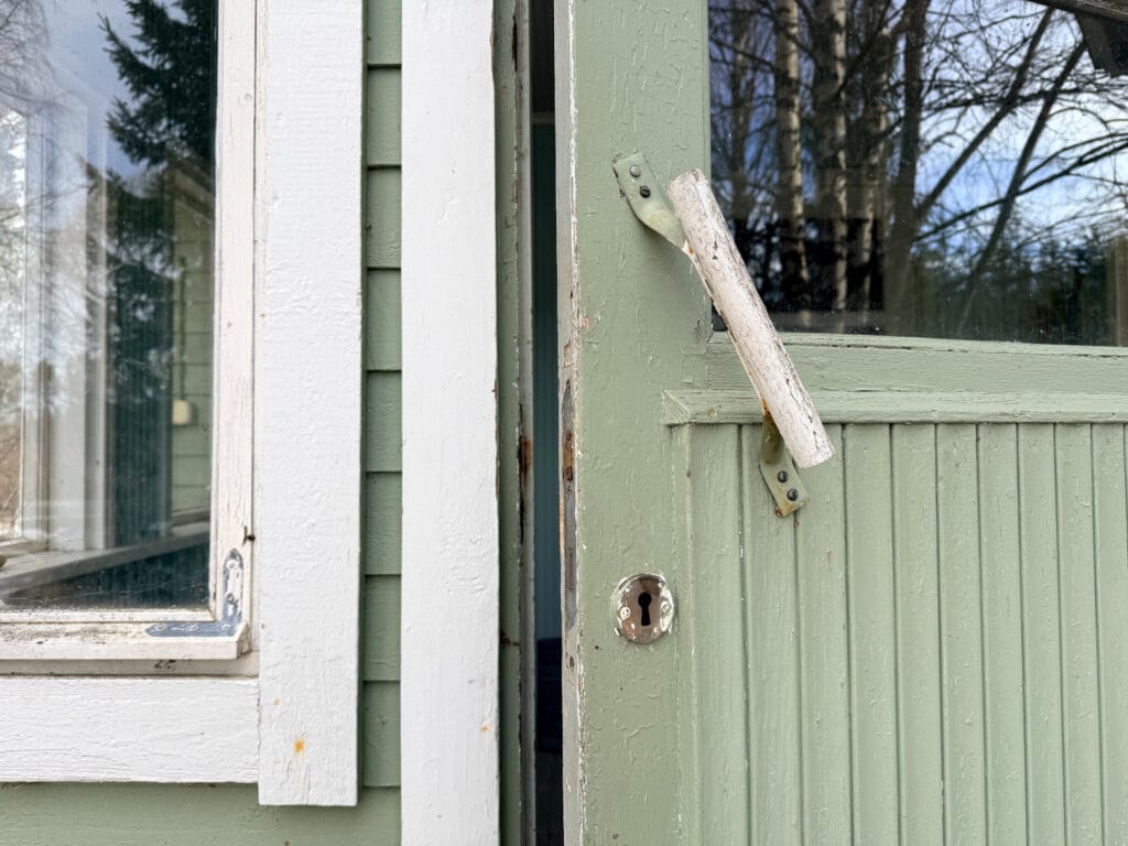 Vaaleanvihreä ovi hieman raollaan. Lähikuva ovesta.