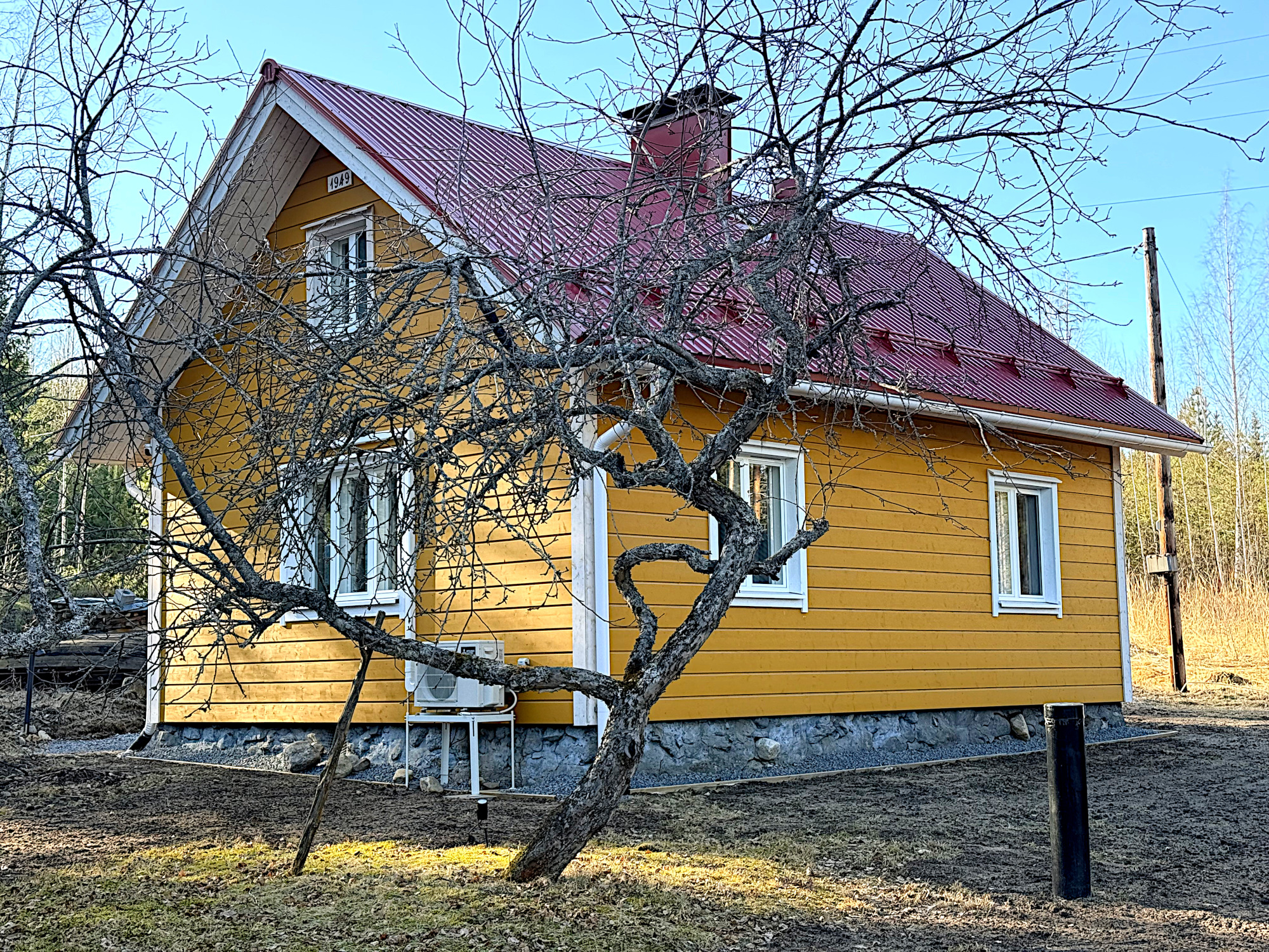 Keltainen, harjakattoinen talo lehdettömän omenapuun takana.