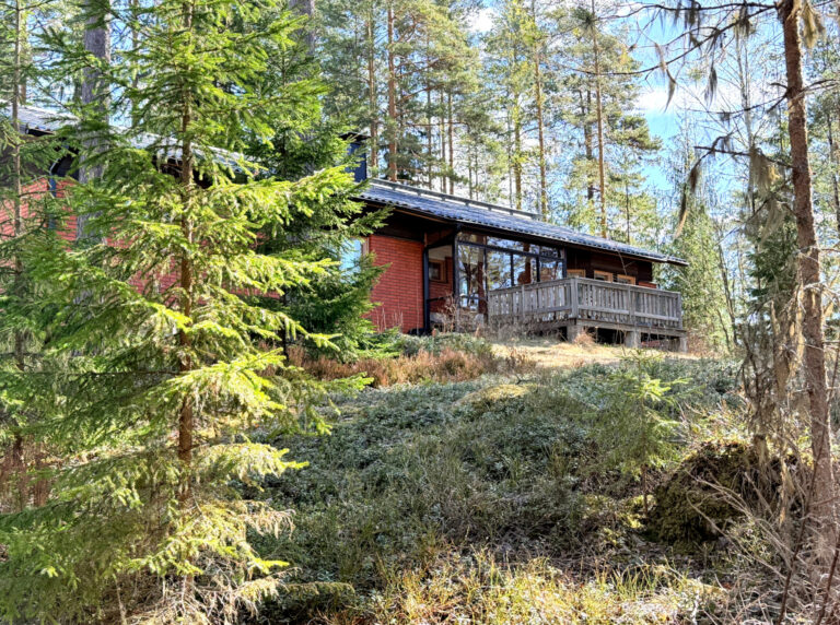 Punatiilinen talo ja terassi metsämaiseman takana.