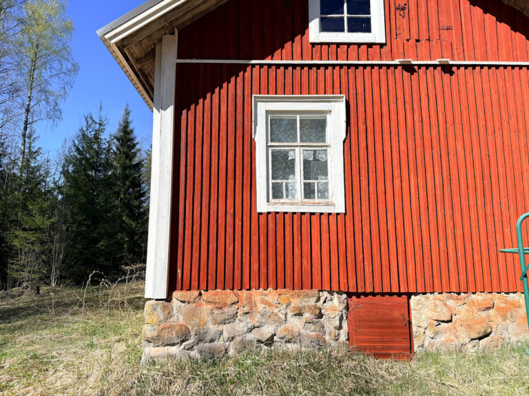 Punainen talo, valkoisin ruutuikkunoin ja nurkkalaudoin.